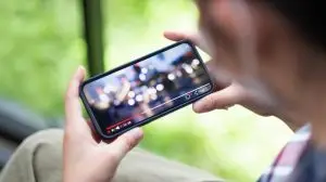 Cropped shot of female hand holding mobile phone playing video stream online.