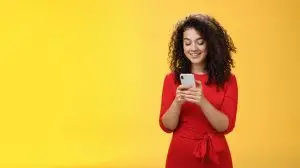 Gil sending message spread news across social network having party inviting friends via smartphone holding mobile phone in hands smiling broadly at device screen as posing over yellow background