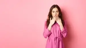 Shocked caucasian woman in light spring dress, gasping and covering mouth with hands, staring with disbelief and shock, standing over pink background