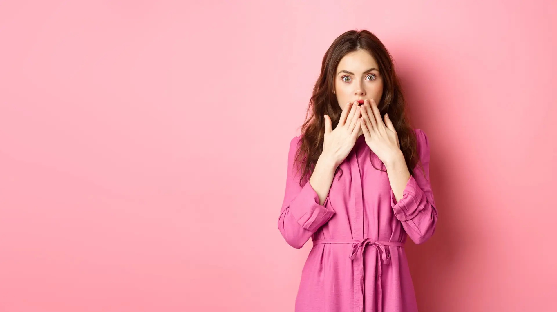 Shocked caucasian woman in light spring dress, gasping and covering mouth with hands, staring with disbelief and shock, standing over pink background
