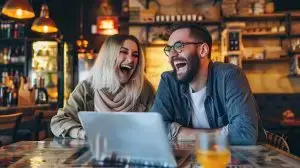 Closeup Young happy white couple bonded laughing using laptop sitting at table on coffee shop