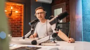 The DJ hosts the program and communicates with the audience on air at the radio station. The announcer reads the news. A male radio host speaks into a microphone and records a podcast