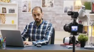 Famous young vlogger typing on laptop while talking