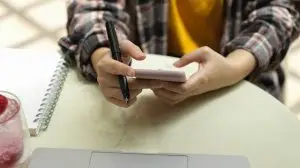 Female holding pen and notebook while working with laptop on coffee table