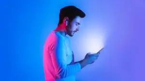 Glow of phone in hands of guy with wireless headphones