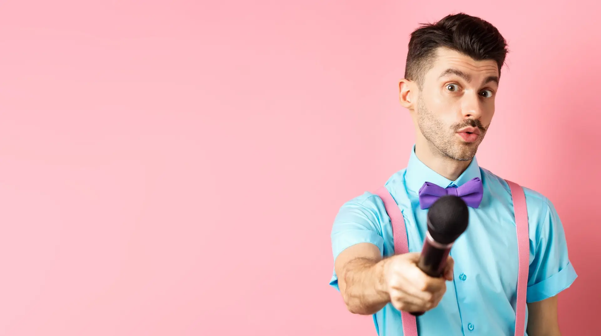 Handsome male show host stretch out hand with microphone, asking for interview or comments, standing on pink background