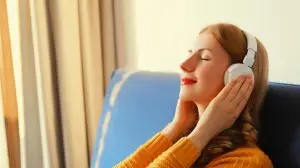 Happy relaxed young woman listening to music with headphones lies on couch at home