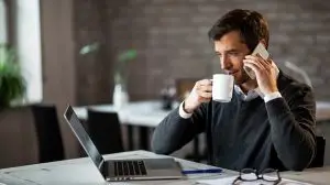 Businessman drinking coffee while talking on the phone and using laptop.