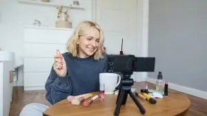 Portrait of blond smiling woman records a lifestyle blog, vlogger or makeup artist recording video for social media, holding mascara, reviewing beauty products for followers online