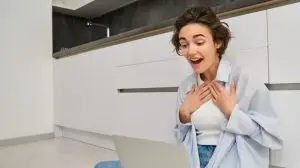 Portrait of girl sitting on floor with laptop, express surprise and excitement, hear amazing news while talking on video chat, having online conversation on her computer