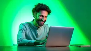 Remote work, online, sales, freelancer. Smiling young guy, salesman holding laptop and working with pleasure over green neon background. Concept of business, sales