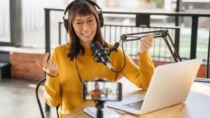 Woman,Podcaster,In,Headphones,And,Glasses,Looking,At,Smartphone,Camera,