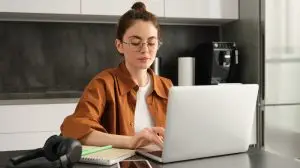 Work and life balance concept. Young woman in glasses, working from home, typing on laptop, student doing homework on computer, sitting in kitchen, freelancing