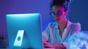 Illuminated Ambition - Businesswoman Working Late at Desk with Vibrant Neon Lights and Deep Blue Background, Creative Workspace Concept