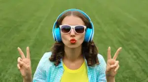 Portrait of happy smiling young woman listening to music in headphones on grass in summer park