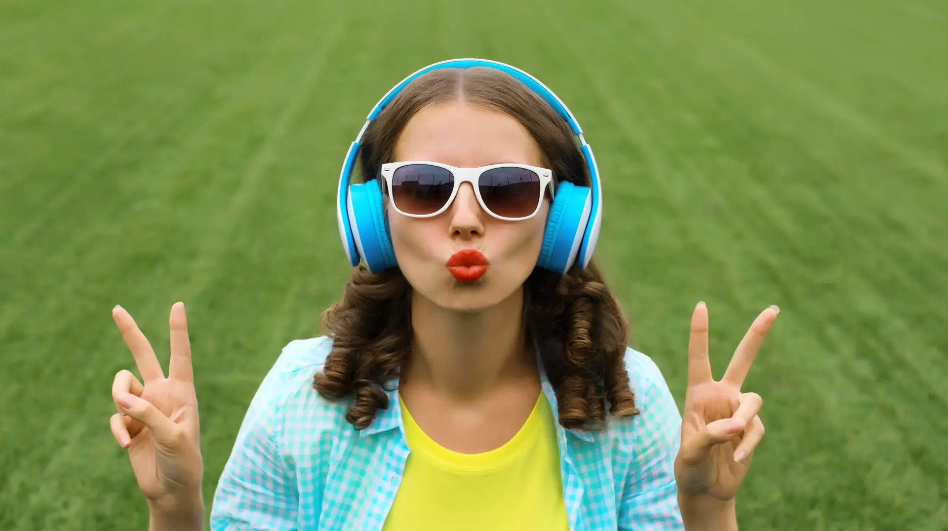 Portrait of happy smiling young woman listening to music in headphones on grass in summer park
