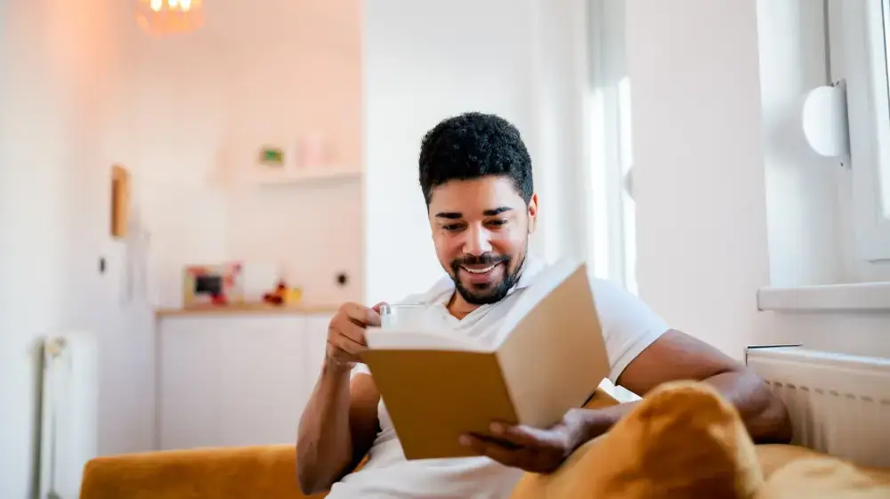 Handsome,Smiling,Man,Reading,A,Book,While,Sitting,On,The