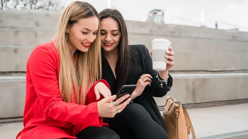 Portrait,Of,Two,Young,Friends,Using,Their,Mobile,Phone,While