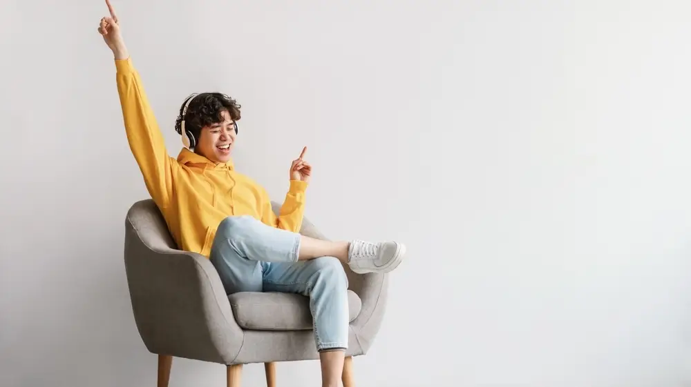 Joyful,Young,Asian,Guy,In,Wireless,Headphones,Sitting,In,Armchair,
