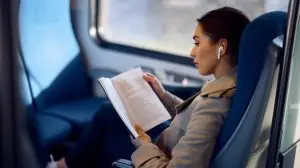 Young,Female,Passenger,Listening,Music,On,Earbuds,And,Reading,Book
