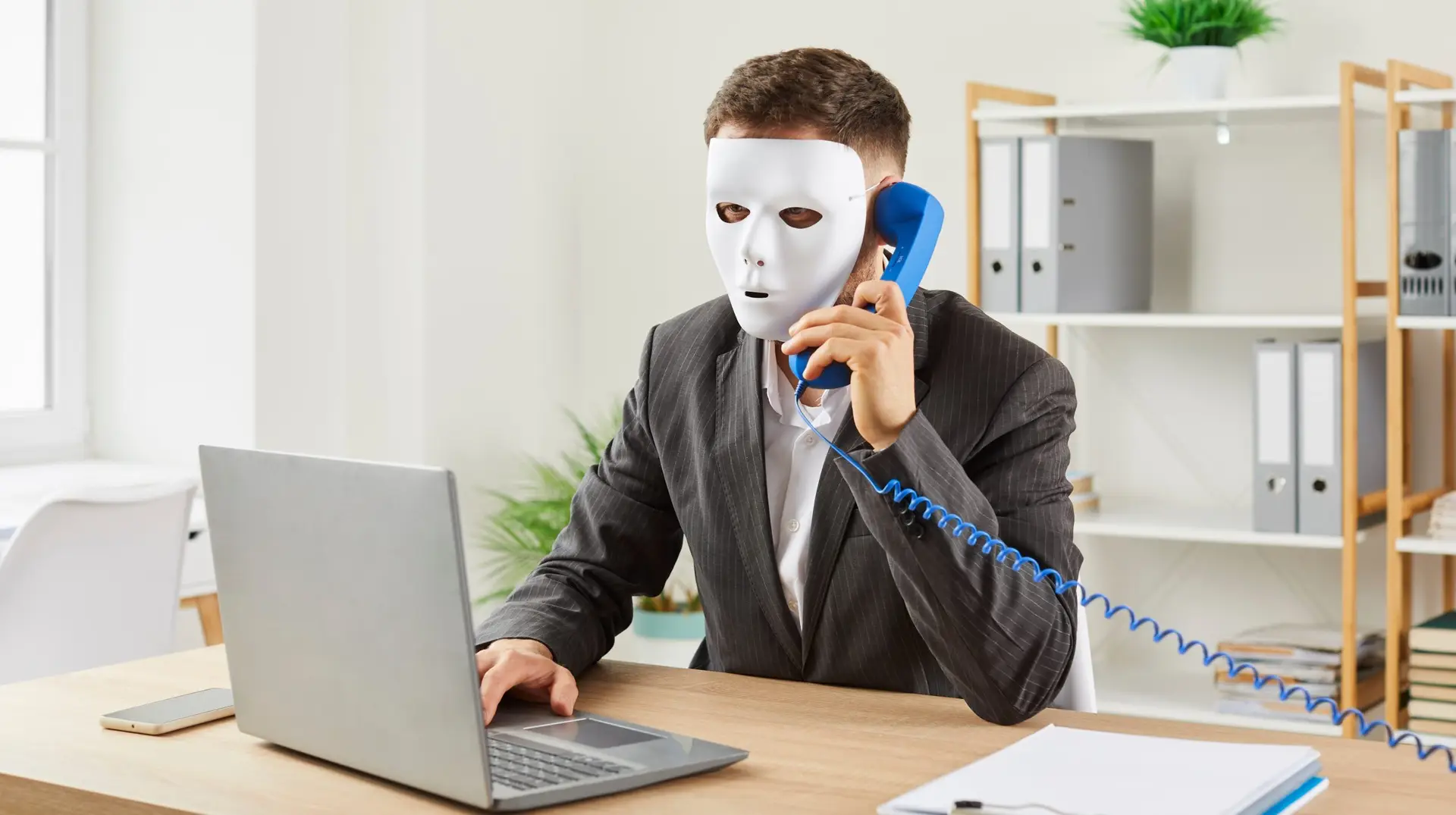 Anonymous,Man,Disguised,In,White,Face,Mask,Sitting,At,Office
