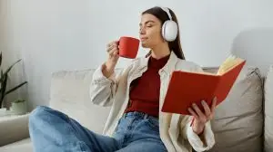 A,Young,Woman,Wearing,Headphones,Sips,Coffee,While,Reading,A