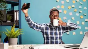 Black,Man,Seated,At,His,Office,Desk,,Drinking,Coffee,And