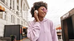 Stylish young curly brunette dark-skinned woman in pink sunglasses and purple hoodie enjoys music i