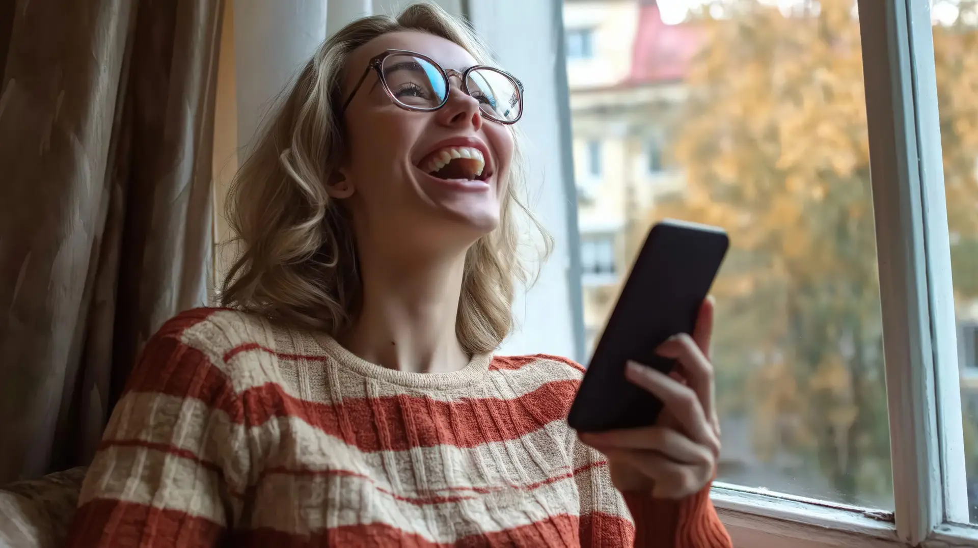 Woman laughing at phone by window
