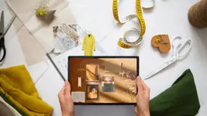 A person is holding a tablet with their online Etsy shop pulled up, in the background we see sewing supplies and plans for new products.