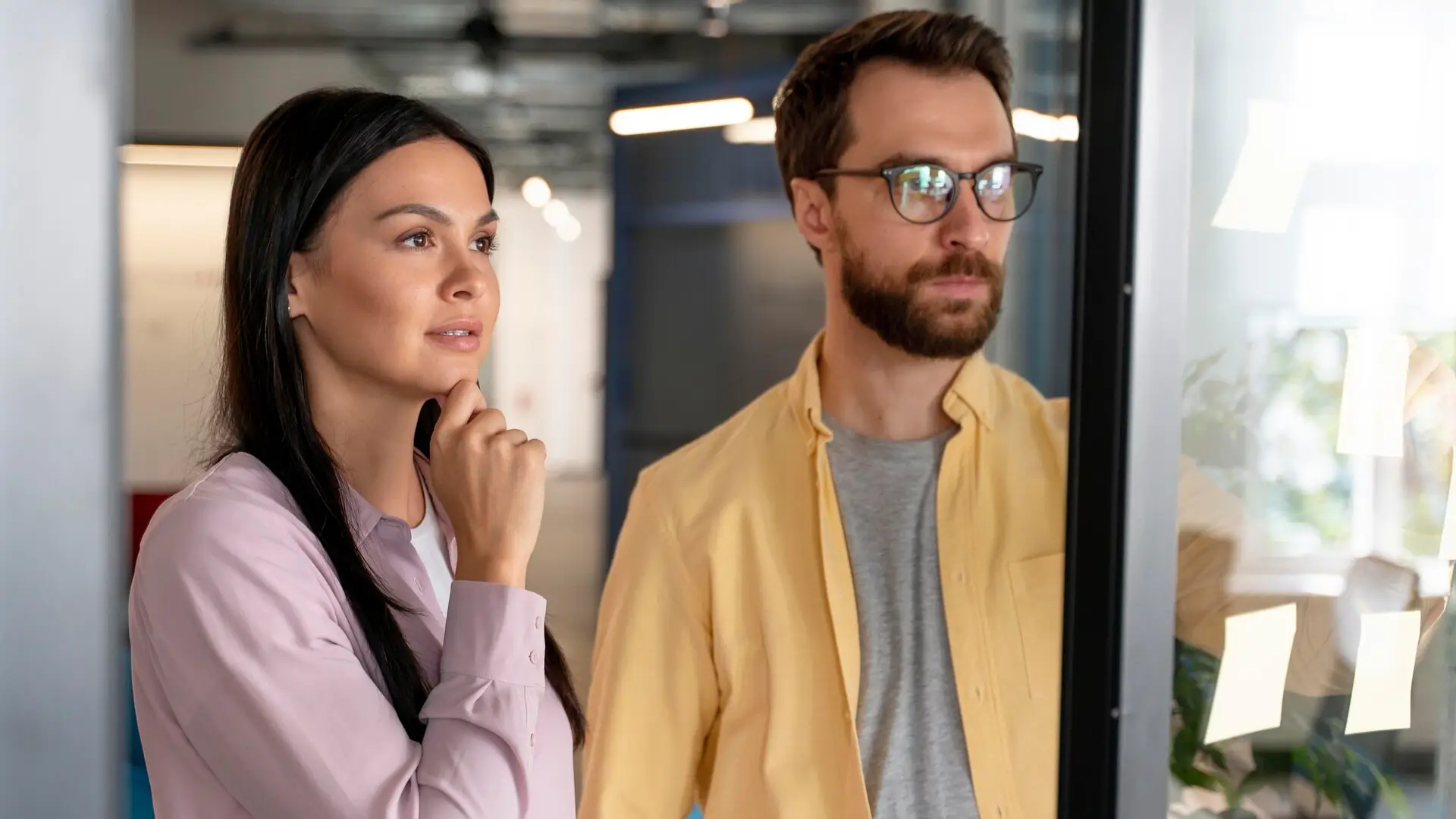 A woman and a man are looking at a bulleting board trying to understand the information about their customers.