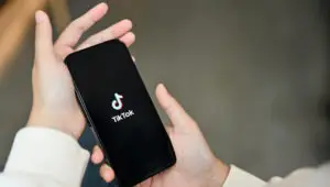 A person holding a smartphone with the TikTok logo on the screen.