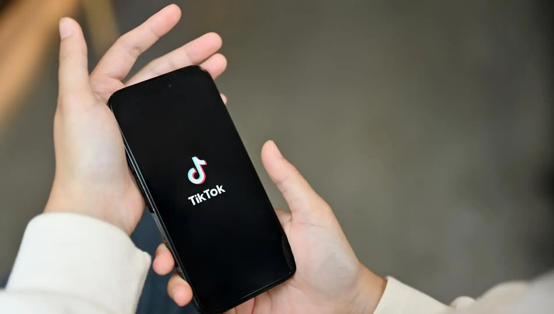 A person holding a smartphone with the TikTok logo on the screen.