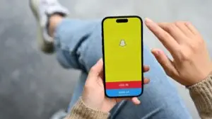 An imager of a woman holding a phone with the Snapchat login page displayed on the screen