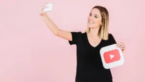 A woman is recording herself with her phone while holding a YouTube logo.