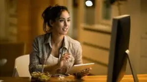 Woman looking at her computer while holding a tablet in her hand