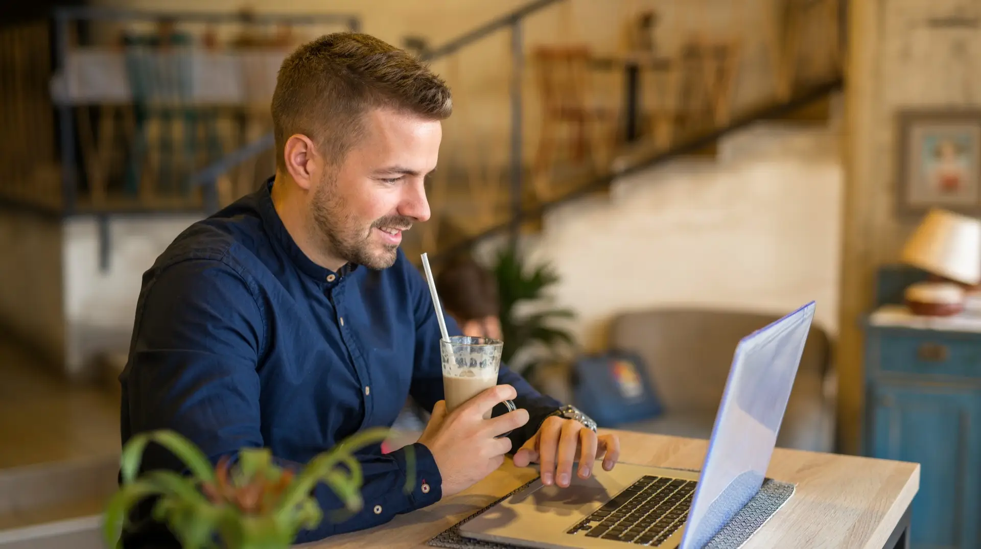 An internet marketer reading the latest issue of Vavoza Insider on his laptop while enjoying an iced coffee